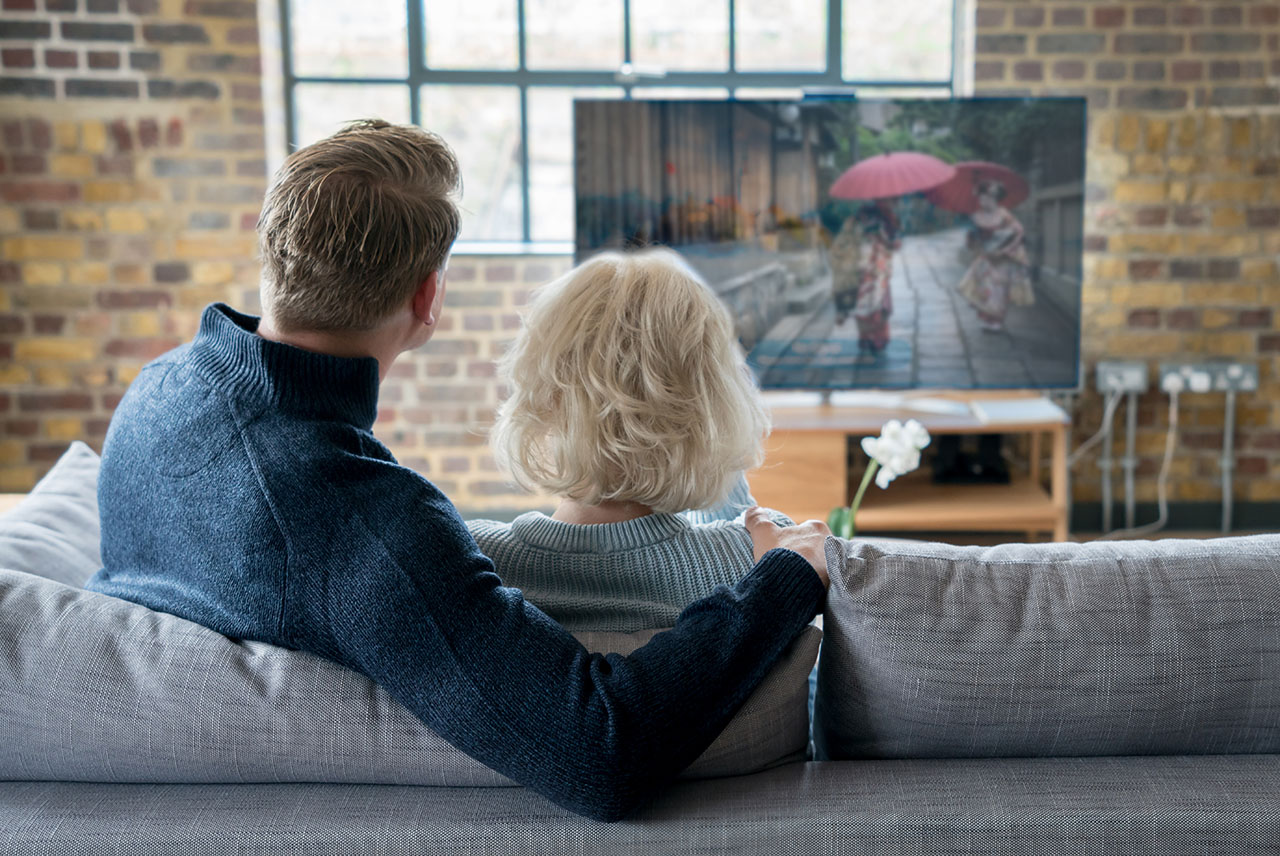 Ein Älteres Paar sitzt auf einer Couch und schaut Fernsehen